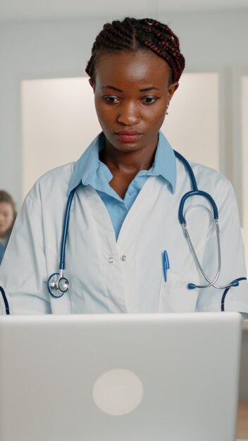 Женщина-врач со стетоскопом, работающая с современным ноутбуком, чтобы вылечить пациента в больничной палате. Медицинский специалист, использующий гаджет для лечения симптомов болезни и болезни с помощью лекарств и лечения