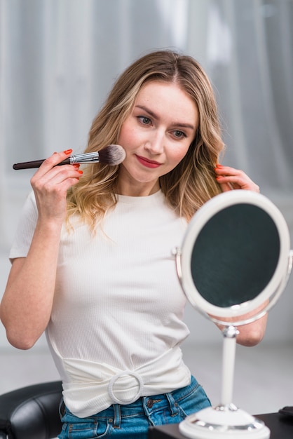 Free photo woman doing makeup in front of mirror