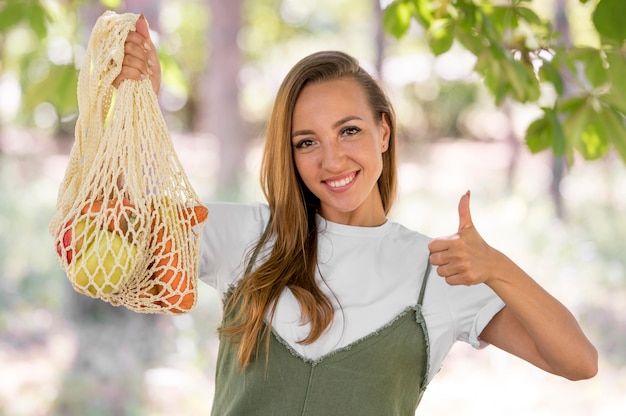 Женщина делает знак "палец вверх" рядом с биоразлагаемым пакетом с вкусностями
