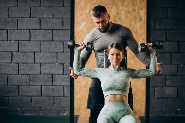 トレーナーとジムでトレーニングをしている女性