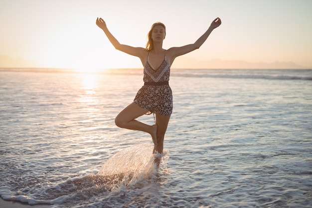 Woman doing yoga at beach during dusk