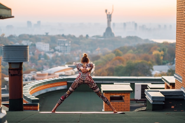 Foto gratuita donna che fa yoga sul tetto di un grattacielo in grande città.