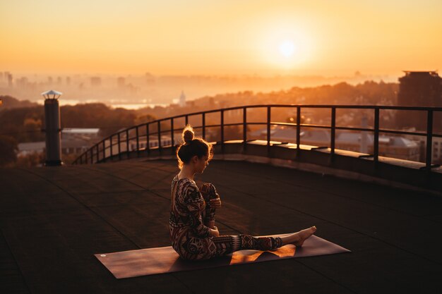 Woman doing yoga on the roof of a skyscraper in big city.