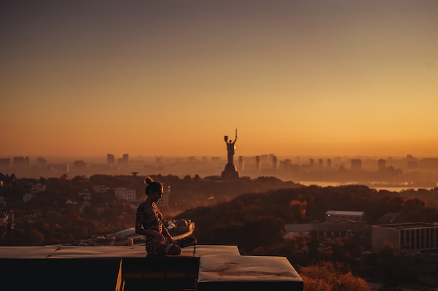 大都会の高層ビルの屋上でヨガをしている女性。
