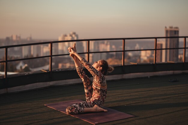 Woman doing yoga on the roof of a skyscraper in big city.