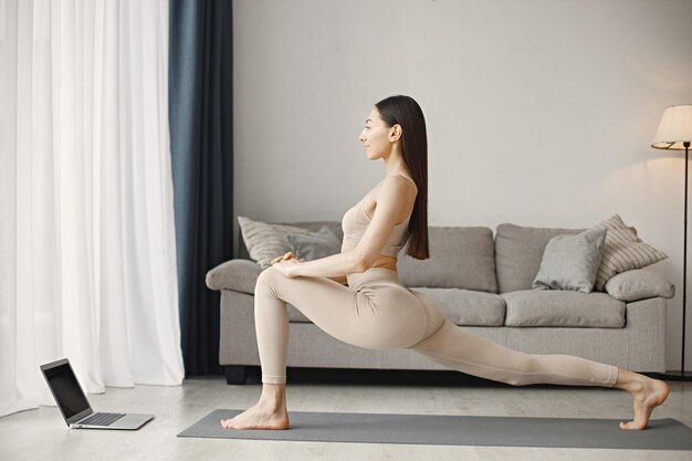 Woman doing yoga while watching online workout tutorials on laptop at home