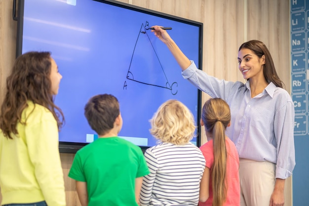 Free photo woman drawing showing triangle on blackboard to children