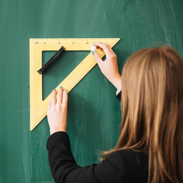 Woman drawing with triangular ruler on blackboard