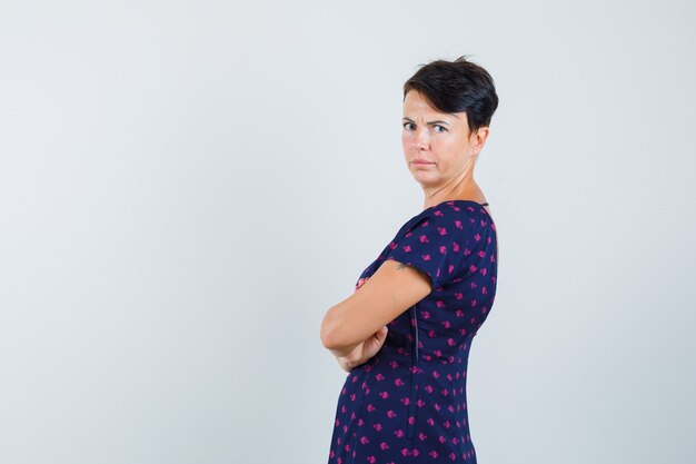 Woman in dress standing with crossed arms and looking serious .