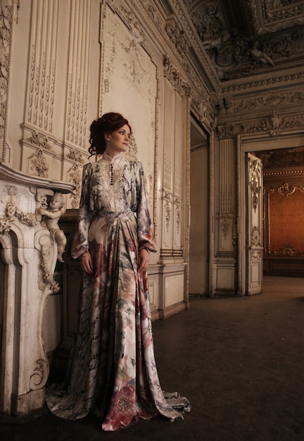 Woman dressed in a dress in the palace posing next to the fireplace