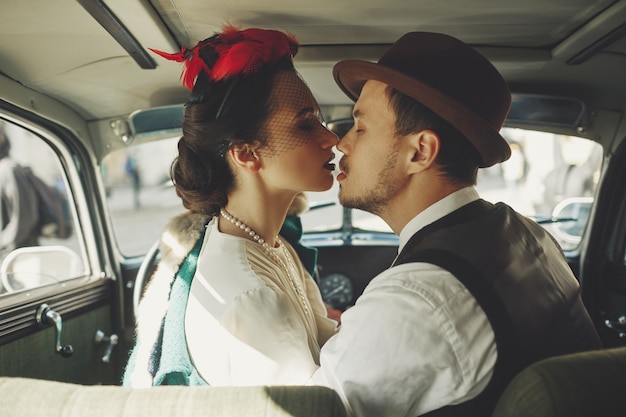 Woman dressed in old-fashioned style sits in a retro car together with her man