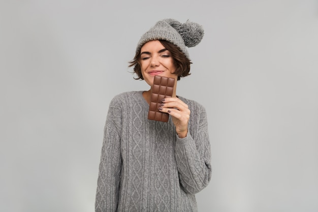 セーターとチョコレートを保持している暖かい帽子に身を包んだ女性。