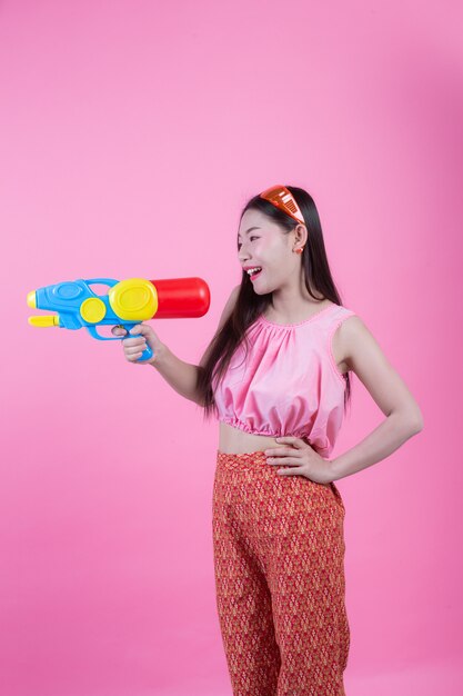 A woman dressed in a traditional Thai folk clothes holding a water gun on a pink background.
