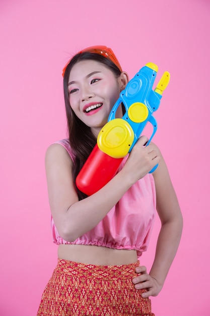 Free photo a woman dressed in a traditional thai folk clothes holding a water gun on a pink background.