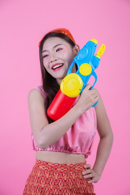 A woman dressed in a traditional Thai folk clothes holding a water gun on a pink background.