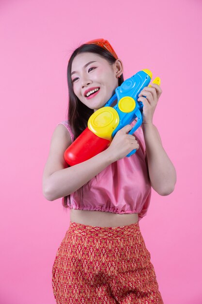 A woman dressed in a traditional Thai folk clothes holding a water gun on a pink background.