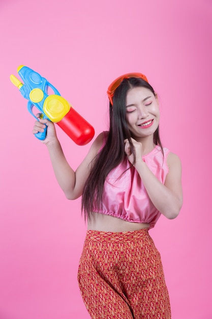 A woman dressed in a traditional Thai folk clothes holding a water gun on a pink background.