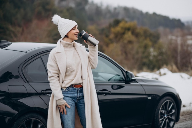 森の道に立っている彼女の車でコーヒーを飲む女性