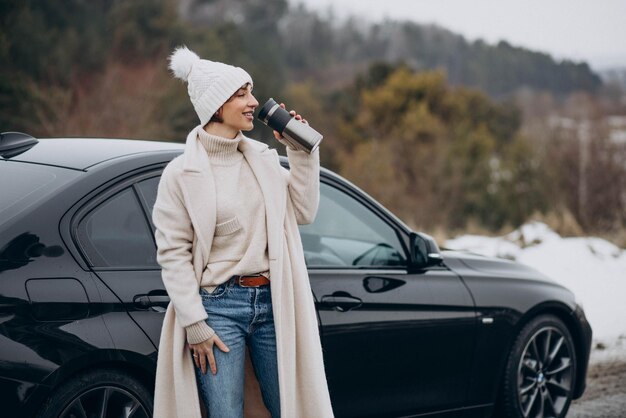 Woman drinking coffee by her car standing on the road in forest