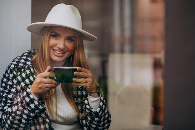 Woman drinking coffee in a cafe, sitting behind the glass