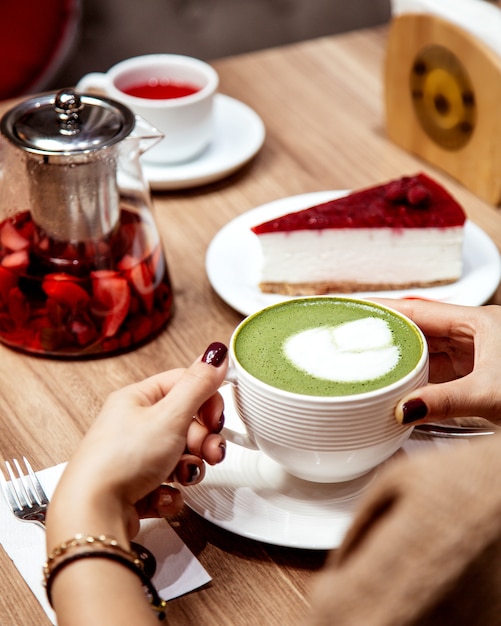 ラテアートと抹茶緑茶のカップを飲む女性