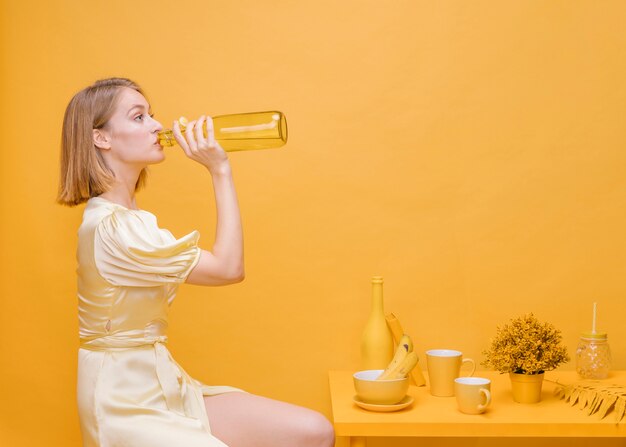 Женщина пьет из бутылки в желтой сцене