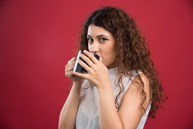 Woman drinking from dark cup on red