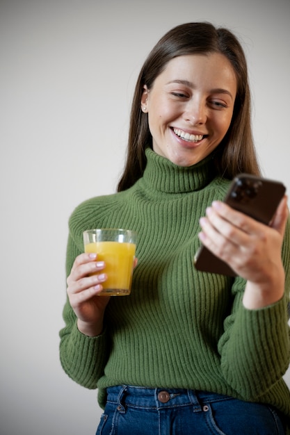 Foto gratuita donna che beve succo mentre guarda il suo smartphone