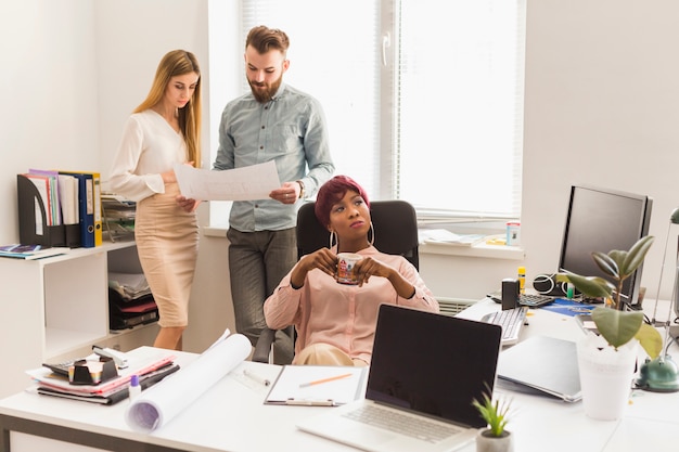 Woman drinking near colleagues with blueprint