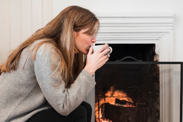 Woman drinking tea near fireplace