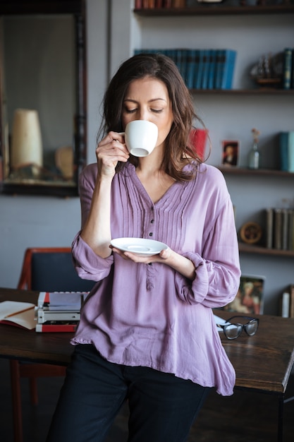 自宅のテーブルにもたれながらお茶を飲む女性