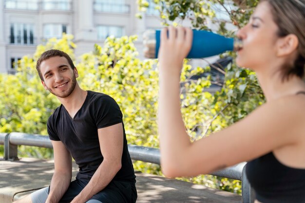 男性と屋外で運動した後、水を飲む女性