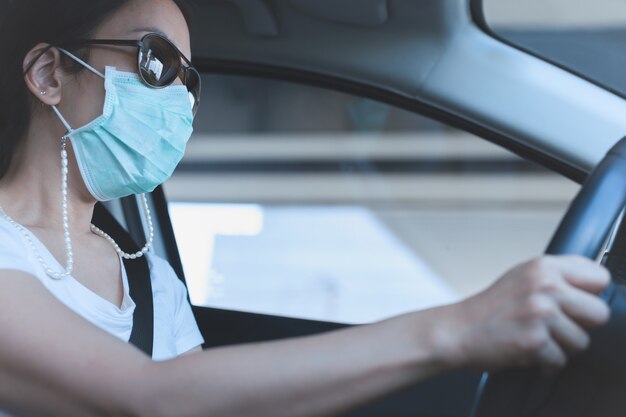 彼女の顔に医療用マスクとサングラスで車を運転している女性ヘルスケアとウイルス対策 プレミアム写真