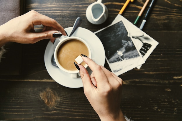 Woman drops sugar in a cup of coffee