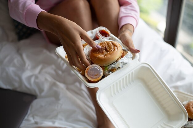 Woman east fast food from delivery on bed in bedroom at home