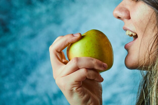 Женщина ест яблоко на голубой стене.