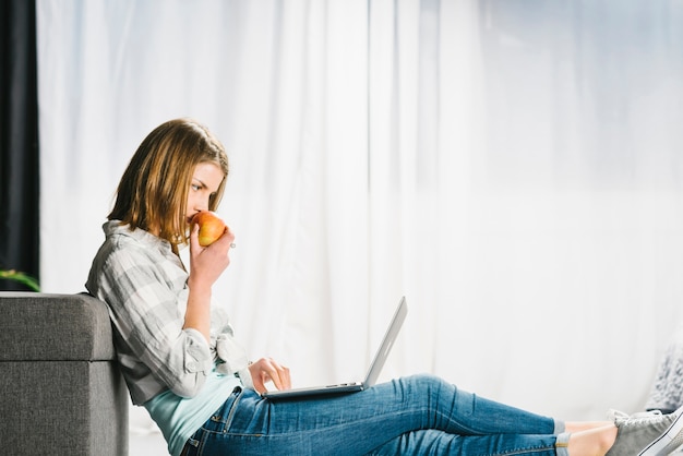 Donna che mangia mela e computer portatile di navigazione