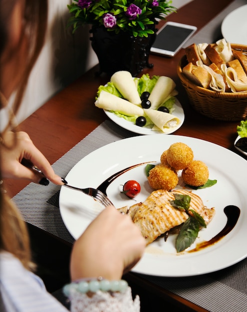Женщина ест запеченное филе лосося с картофелем и сырными рулетами и овощами микс.