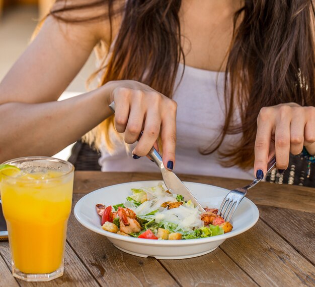 新鮮なオレンジジュースのガラスとシーザーサラダを食べる女性