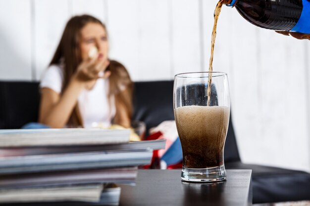 ソファーに座って、チップを食べる女性。ソーダのFosucガラス。