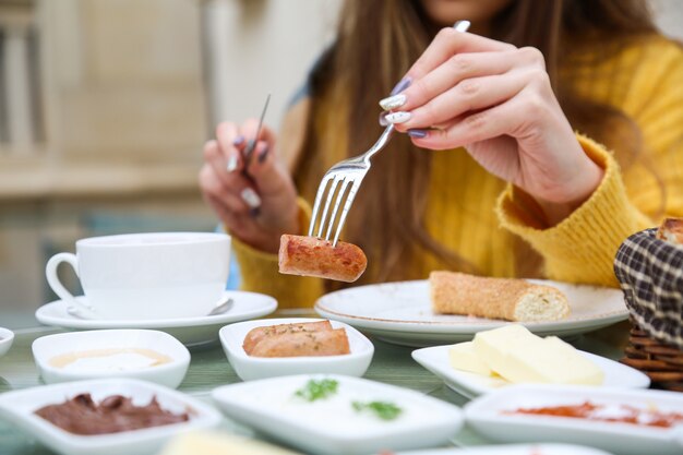 Woman eating fried sausages while breakfast close up view