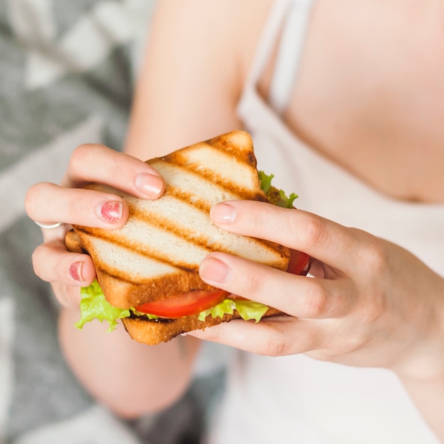 手に焼きサンドイッチを食べる女性