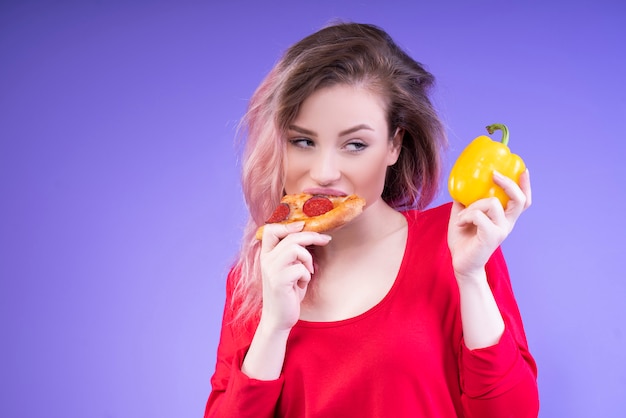 Woman eating pizza looks at the yellow pepper in her hand
