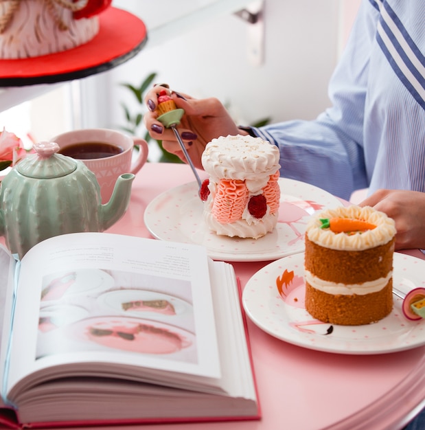 Woman eating portioned meringue cake with pink cream and raspberry