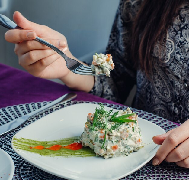 woman eating portioned olivier salad with dill on top at the restaurant