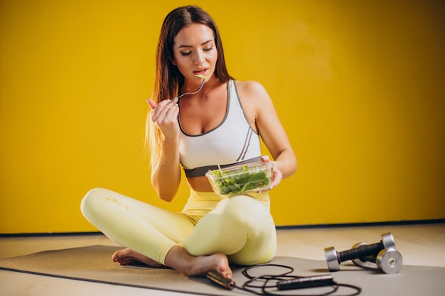 Woman eating salad isolated on yellow background