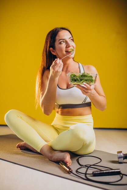 黄色の背景に分離されたサラダを食べる女性