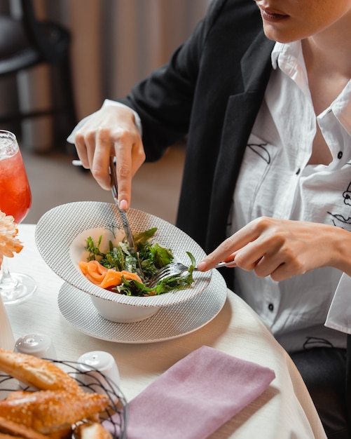 женщина ест салат с копченым лососем с рукколой и укропом в ресторане