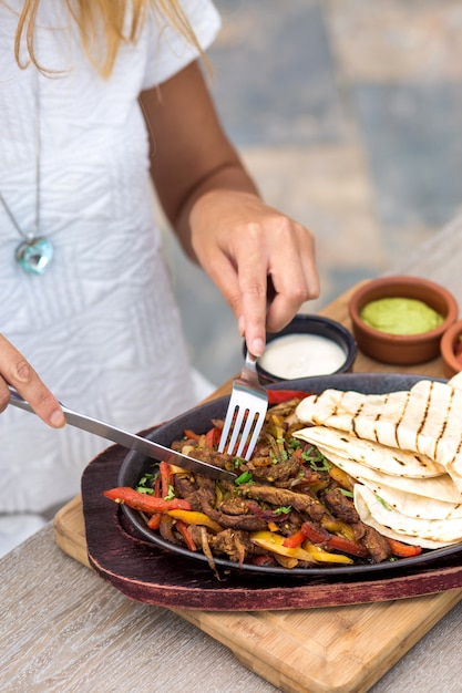 Woman eating stir-fried lamb with colorful bell peppers, served with flatbread