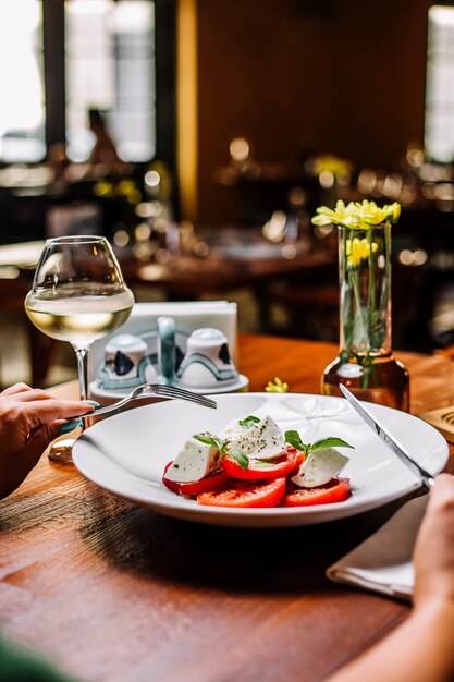 Woman eating tomato salad with mozzarella and mint served with white wine